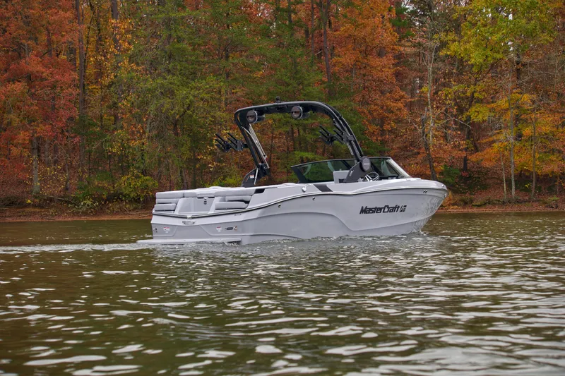 Slide: The Image of 2025 MasterCraft XT23 boat cruising on a lake with autumn foliage backdrop. - 5