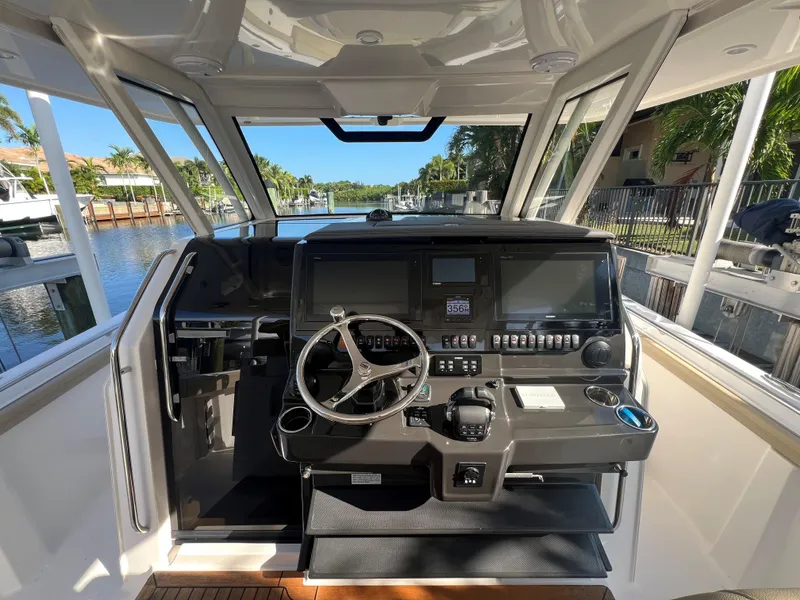 Slide: The Image of 2020 Pursuit S408 boat helm with modern controls and steering wheel, docked by a scenic canal. - 14
