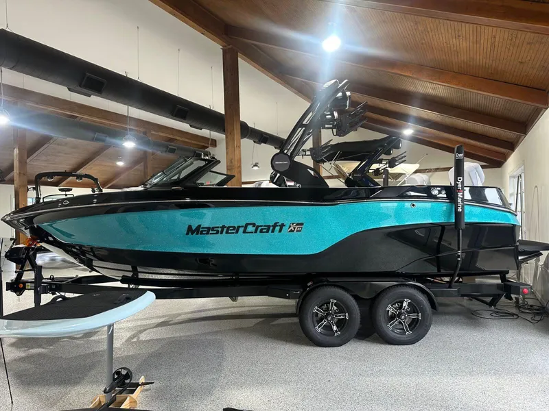 The Image of 2025 MasterCraft XT23 boat in showroom, vibrant teal and black design. - 0