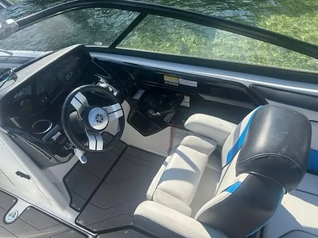 Slide: The Image of 2019 Yamaha Boats 212X cockpit with steering wheel and seating, on clear water. - 8