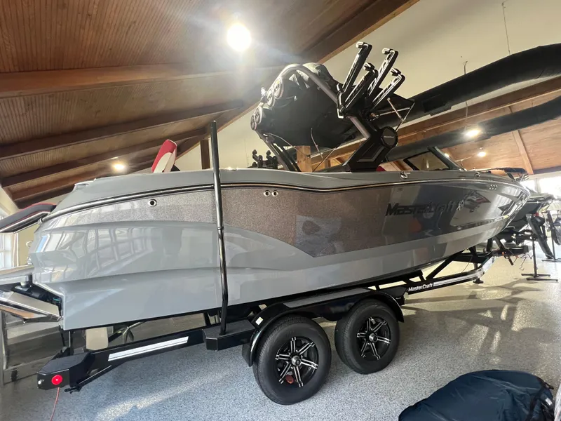 Slide: The Image of 2025 MasterCraft X24 boat on trailer in showroom, sleek gray design. - 2