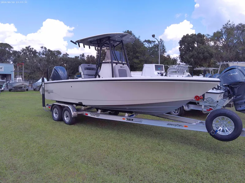 Slide: The Image of 2025 Pathfinder 2400 Open boat on trailer, parked on grass with trees in background. - 2