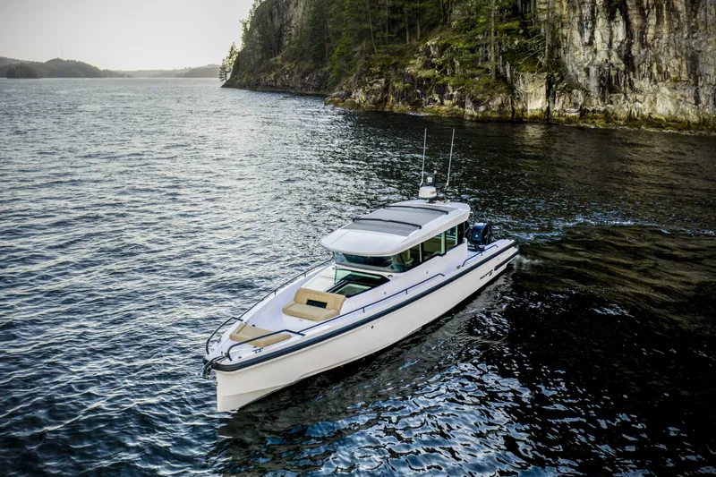 Slide: The Image of 2025 Axopar 37 XC CROSS CABIN cruising near rocky shoreline. - 2