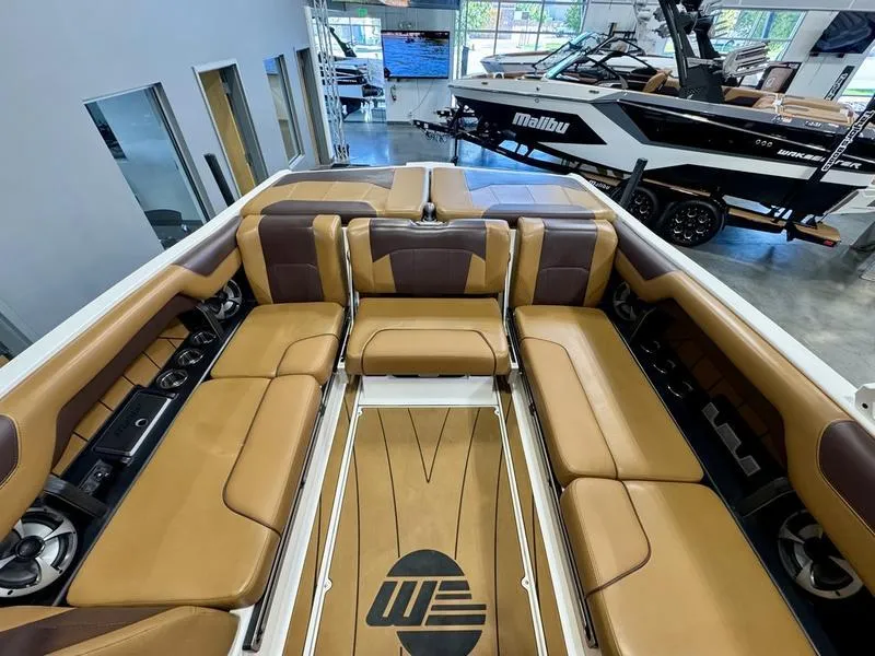 Slide: The Image of 2021 Malibu 25 LSV boat interior with tan and brown seating in showroom. - 15