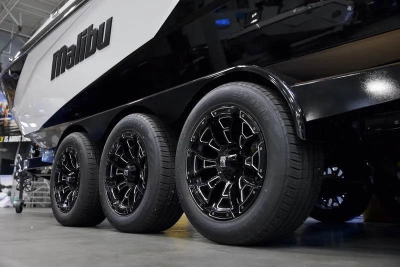 Slide: The Image of 2025 Malibu 26 LSV boat on triple-axle trailer with sleek black wheels. - 8