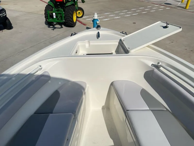 Slide: The Image of 2024 Mako 214 CC boat interior with open storage compartment, docked near green tractor. - 4