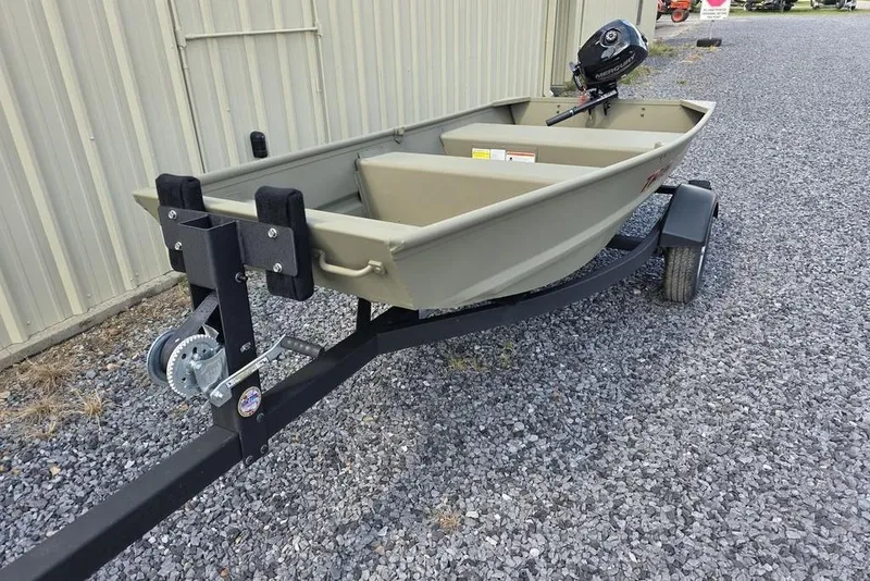 Slide: The Image of 2025 Tracker Grizzly 10 Jon boat on trailer, parked on gravel near a building. - 2
