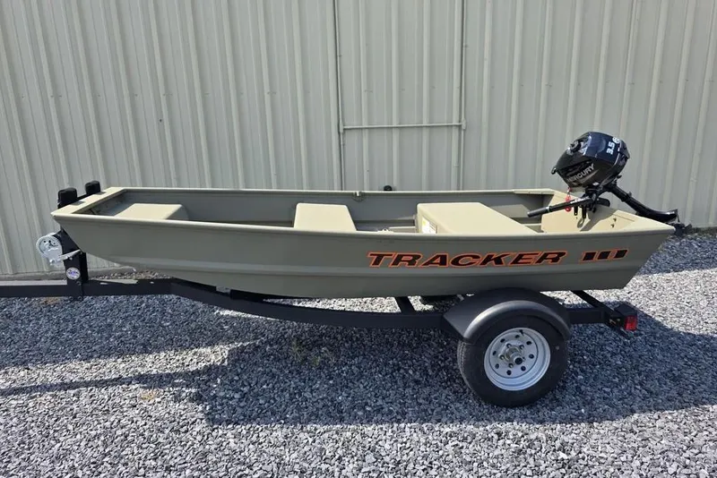 Slide: The Image of 2025 Tracker Grizzly 10 Jon boat on trailer, parked on gravel, with outboard motor. - 4