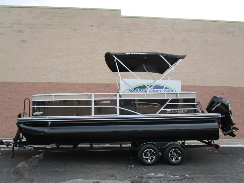 The Image of 2024 Ranger Reata 223C pontoon boat with black canopy on a trailer. - 1