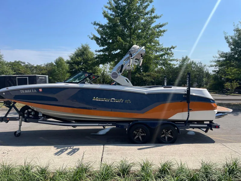 Slide: The Image of 2021 MasterCraft NXT 24 boat on trailer, parked outdoors, side view. - 2
