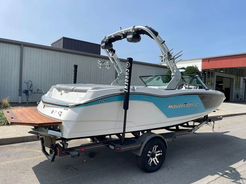 Slide: The Image of 2018 MasterCraft NXT20 boat on trailer, parked outdoors near industrial building. - 2