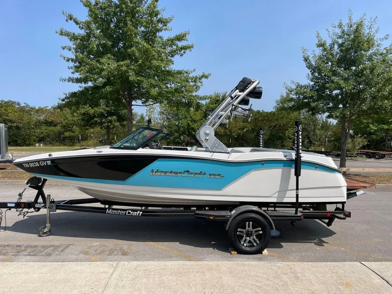 Slide: The Image of 2018 MasterCraft NXT20 boat on trailer, parked outdoors with trees in the background. - 5