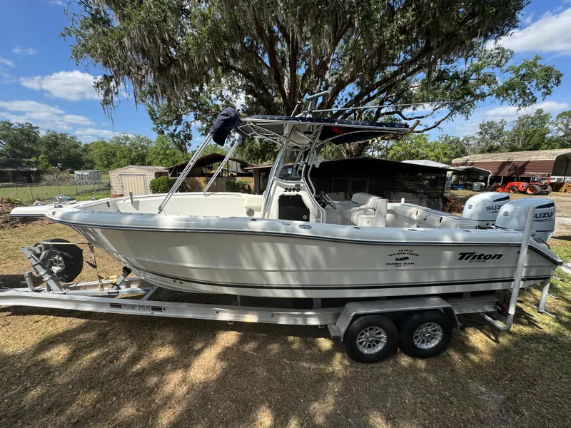 Slide: The Image of 2003 Triton 2690 CC boat on trailer, parked outdoors under a tree. - 12