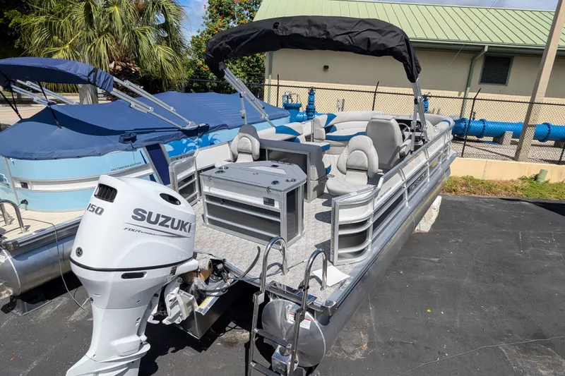Slide: The Image of 2026 Trifecta 22TRFC LE pontoon boat with Suzuki 150 engine, docked outdoors. - 2
