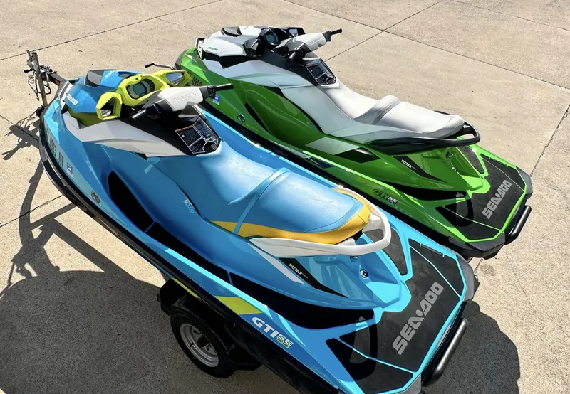 Slide: The Image of Two 2015 Sea-Doo GTI SE 130 jet skis, blue and green, parked on a trailer. - 2
