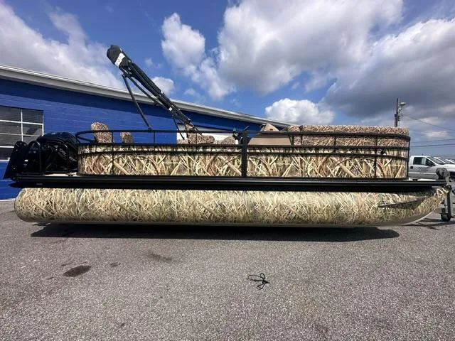 The Image of 2025 Starcraft LX 22 F pontoon boat with camouflage design, parked outdoors under a cloudy sky. - 0