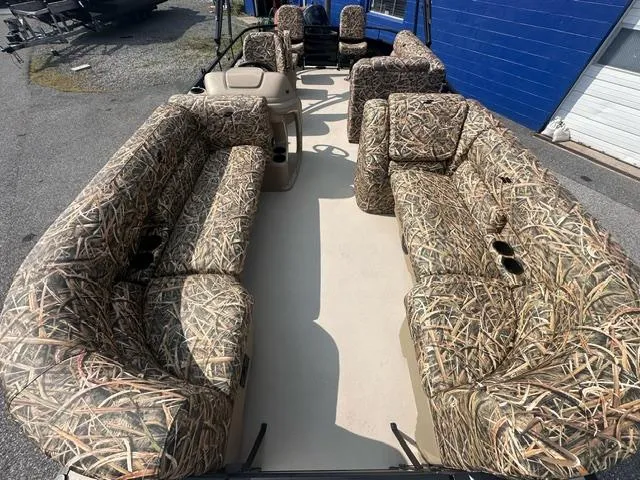 Slide: The Image of 2025 Starcraft LX 22 F pontoon boat with camouflage seating, docked outdoors. - 2