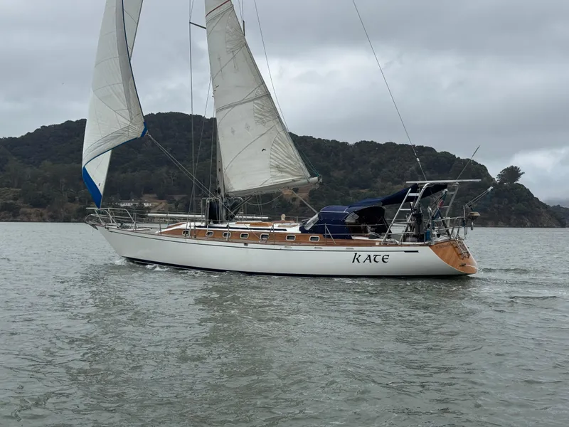Slide: The Image of 1983 Tayana 52 Aft Cockpit sailboat on water, sails up, overcast sky, scenic background. - 7