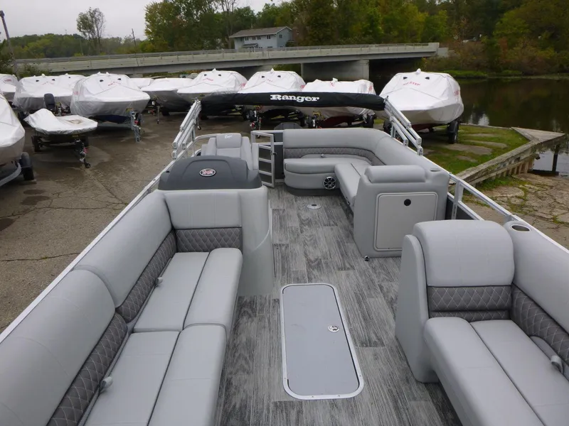 Slide: The Image of 2024 Ranger Reata 223C pontoon boat with spacious seating, docked near covered boats. - 11