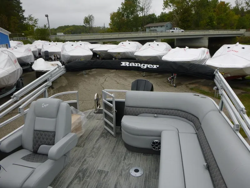 Slide: The Image of 2024 Ranger Reata 223C pontoon boat with gray seating, docked near covered boats. - 18