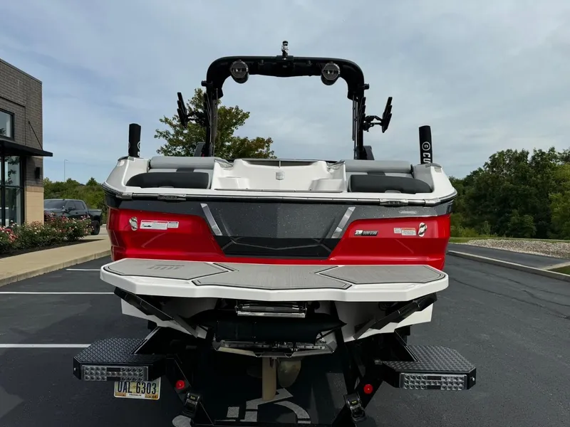Slide: The Image of 2022 MasterCraft X24 boat, red and white, parked on asphalt with trees in background. - 5