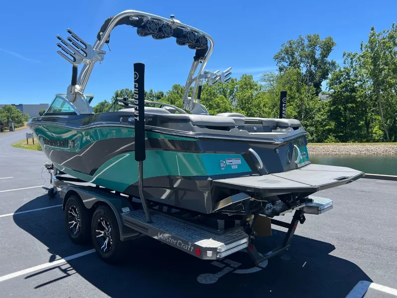 Slide: The Image of 2017 MasterCraft XT21 boat on trailer, parked outdoors, with wakeboard tower and vibrant design. - 7