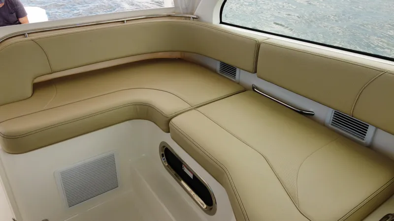 Slide: The Image of 2020 Pursuit OS 385 Offshore boat interior with beige seating and window view. - 20