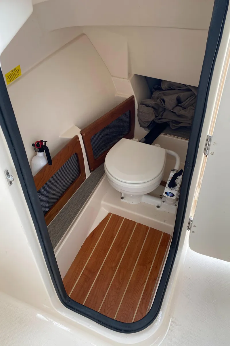 Slide: The Image of 2022 Grady-White Freedom 235 boat interior with compact marine toilet and wooden flooring. - 13