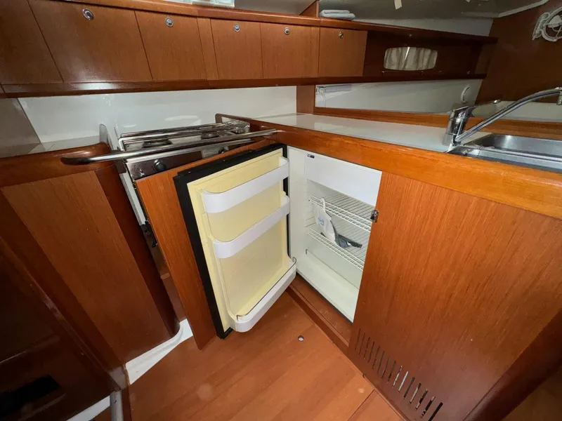 Slide: The Image of 2008 Beneteau Oceanis 37 yacht kitchen with open fridge and wooden cabinetry. - 37