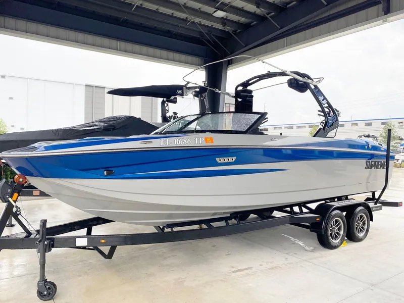Slide: The Image of 2023 Supreme S240 boat in blue and white on a trailer under a shelter. - 1