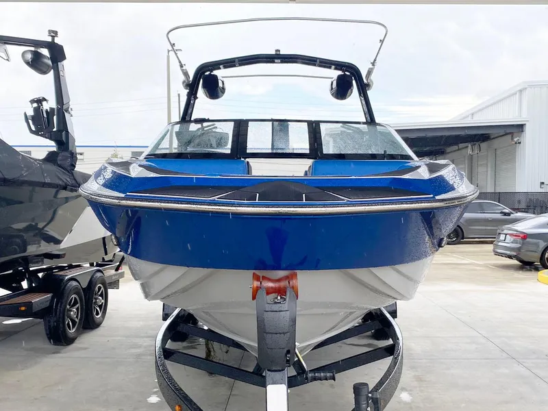 Slide: The Image of 2023 Supreme S240 boat in blue, parked on a trailer at a marina. - 2