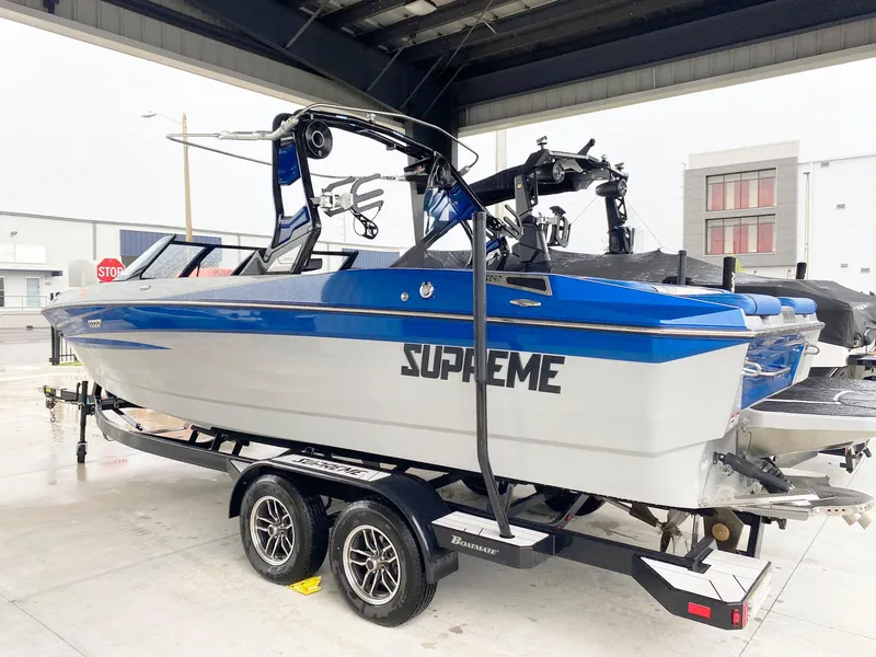 Slide: The Image of 2023 Supreme S240 boat on trailer, blue and white design, under shelter. - 4