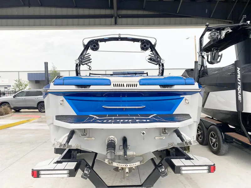 Slide: The Image of 2023 Supreme S240 boat, blue and white, rear view in a showroom. - 5