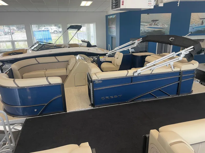 Slide: The Image of 2024 Crest 200L Classic LX pontoon boat in showroom, featuring blue exterior and beige seating. - 2