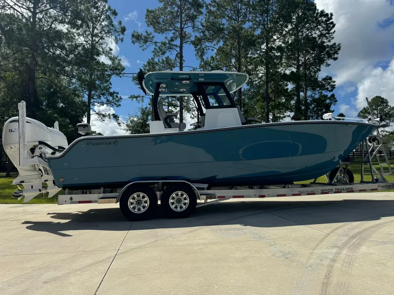Slide: The Image of 2024 Freeman 28 boat on trailer, parked outdoors with trees in background. - 0