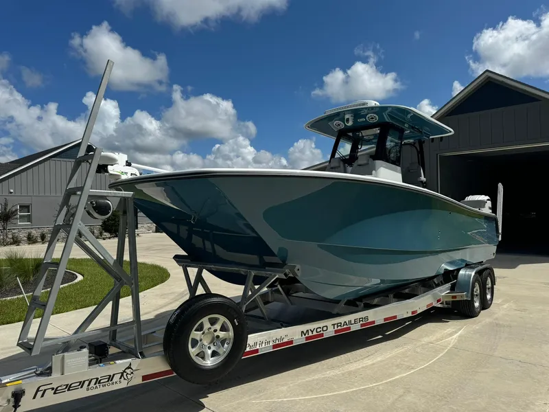 Slide: The Image of 2024 Freeman 28 boat on trailer, parked outdoors under a clear blue sky. - 2