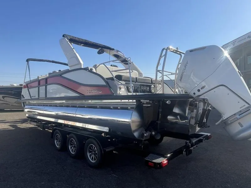 Slide: The Image of 2025 Harris Grand Mariner SL 250 pontoon boat with triple-axle trailer, parked outdoors. - 5