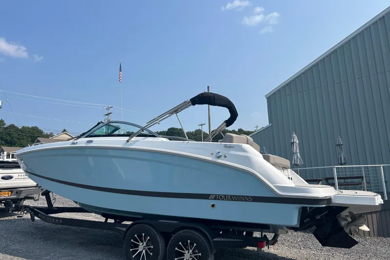Slide: The Image of 2025 Four Winns HD3 boat on trailer, parked outdoors near a metal building. - 2