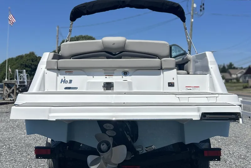 Slide: The Image of 2025 Four Winns HD3 boat rear view with propeller, parked on gravel, under clear blue sky. - 8