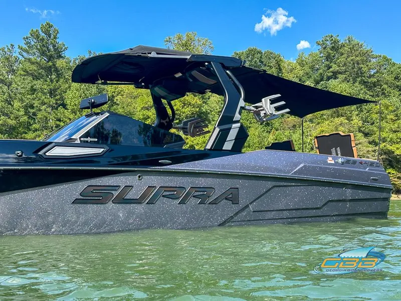 Slide: The Image of 2024 Supra SE boat on a lake with lush green trees in the background. - 5
