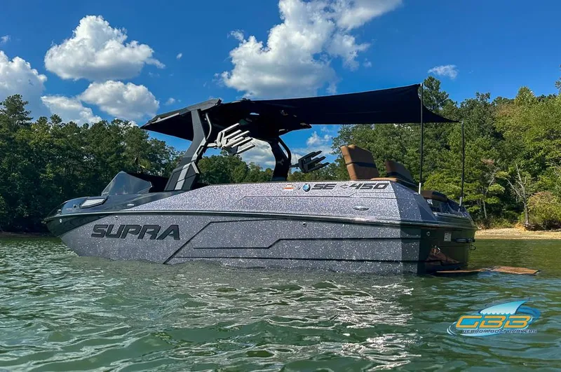 Slide: The Image of 2024 Supra SE boat on a lake, featuring sleek design and canopy, surrounded by trees. - 6