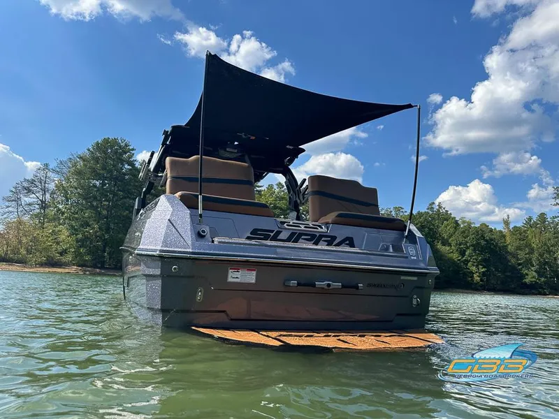 Slide: The Image of 2024 Supra SE boat on water, rear view, under blue sky with trees in background. - 8