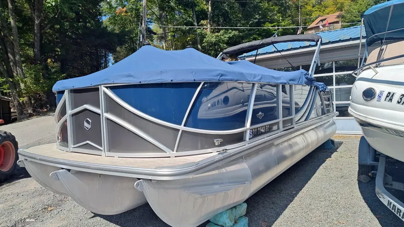 Slide: The Image of 2023 South Bay 523E 2.75 pontoon boat with blue cover, parked outdoors. - 1