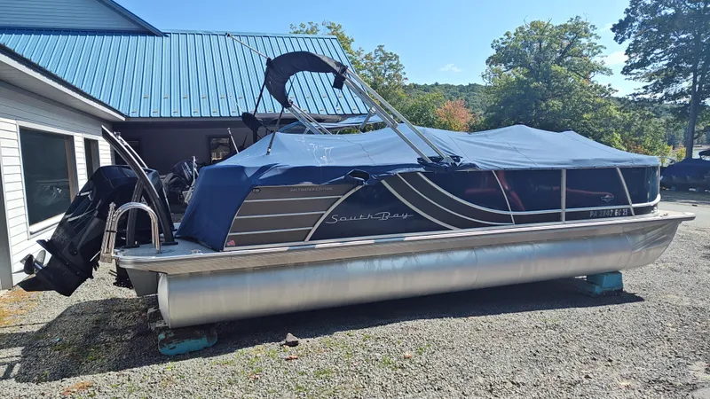 Slide: The Image of 2023 South Bay 523E 2.75 pontoon boat with blue cover, parked outdoors. - 4