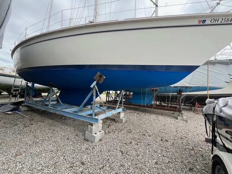 Slide: The Image of 1986 Pearson 36 sailboat on a stand, blue hull, gravel ground. - 8