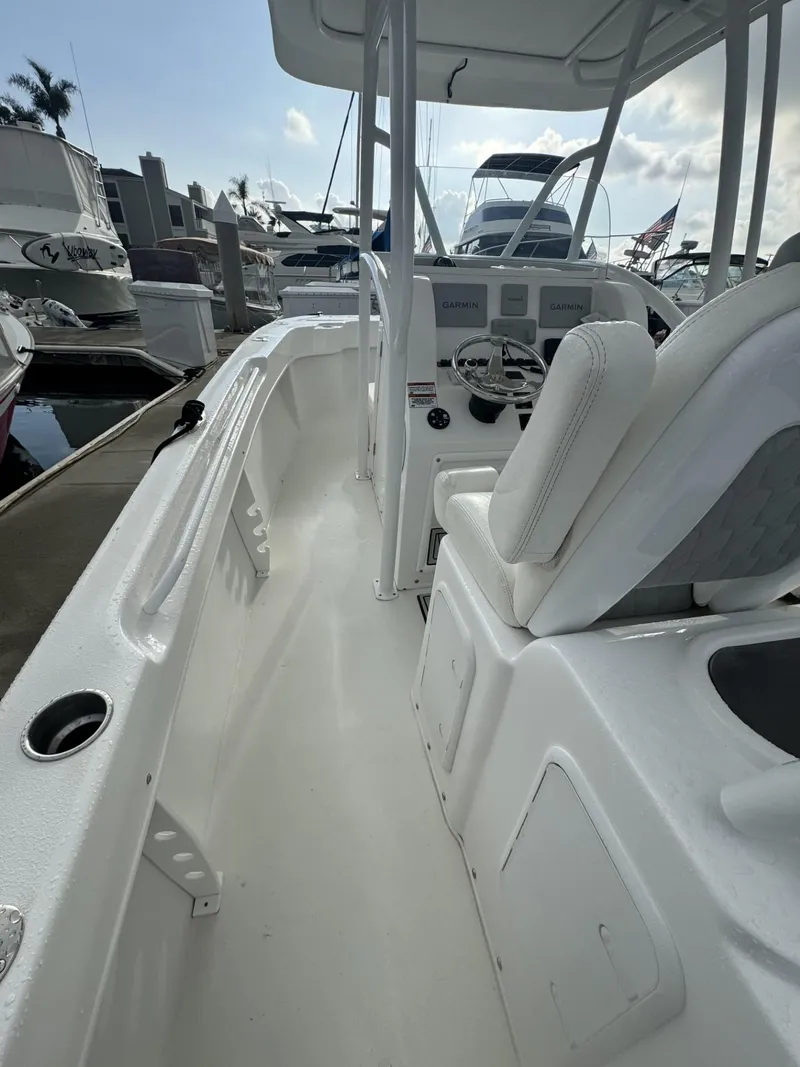 Slide: The Image of 2021 Twin Vee Catamaran interior with white seating and steering console at a marina. - 10