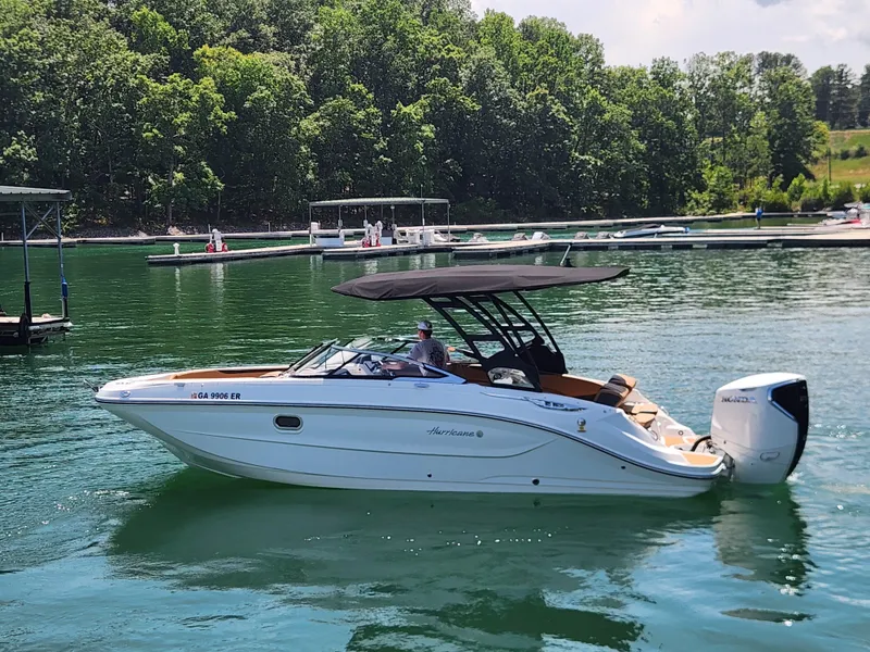 Slide: The Image of 2024 Hurricane SunDeck 2600 OB boat cruising on a scenic lake with lush greenery. - 2