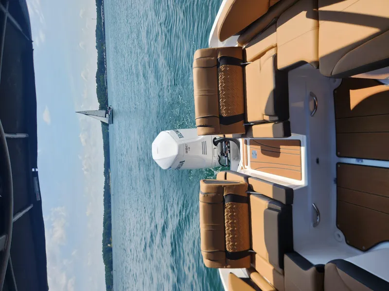 Slide: The Image of 2024 Hurricane SunDeck 2600 OB on serene water with sailboat in background. - 8