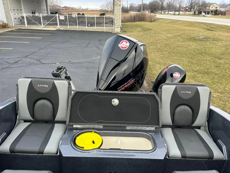 Slide: The Image of 2025 Lund 189 Tyee GL boat interior with seating and motor, parked outdoors. - 14