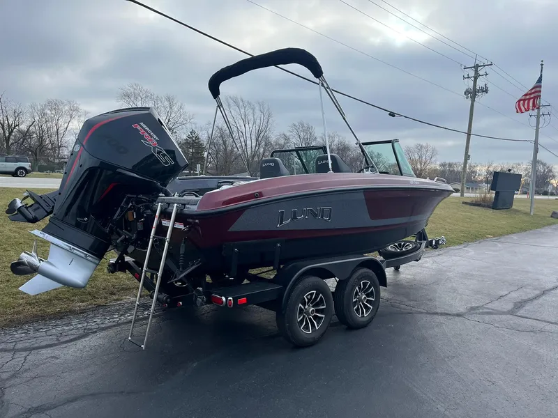 Slide: The Image of 2025 Lund 189 Tyee GL boat on trailer with outboard motor, parked outdoors. - 25